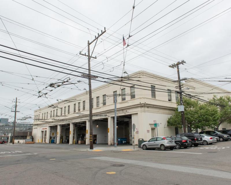 Bus yard entrance with parked cars along the building side up the hill 