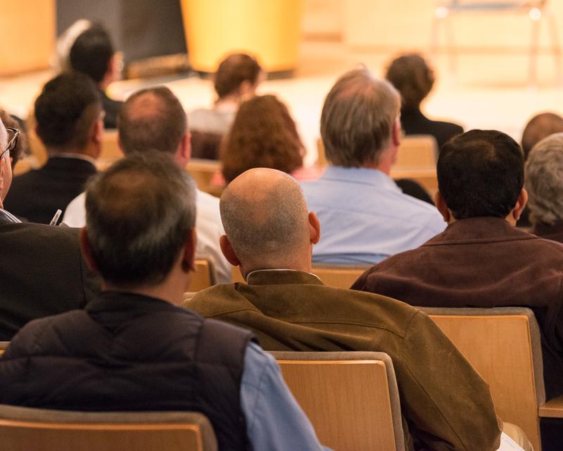 photo showing the back of several people seated in an auditorium