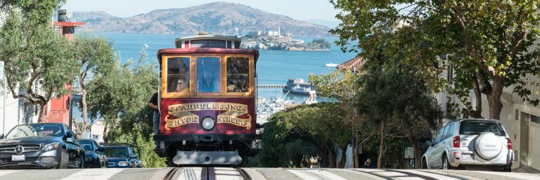 cable car cresting hyde street hill with bay, angel island, and alcatraz island in background