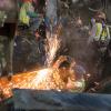 A metalworker cleans up the ends of a large steel I-beam for welding, which will be used as a bracket at the south headwall.