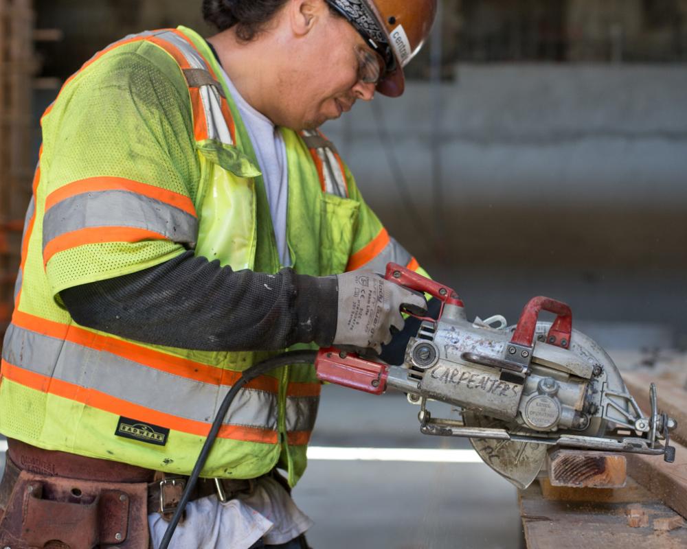 A carpenter cuts a 2x4 as part of concrete form assembly inside the YBM station headhouse.