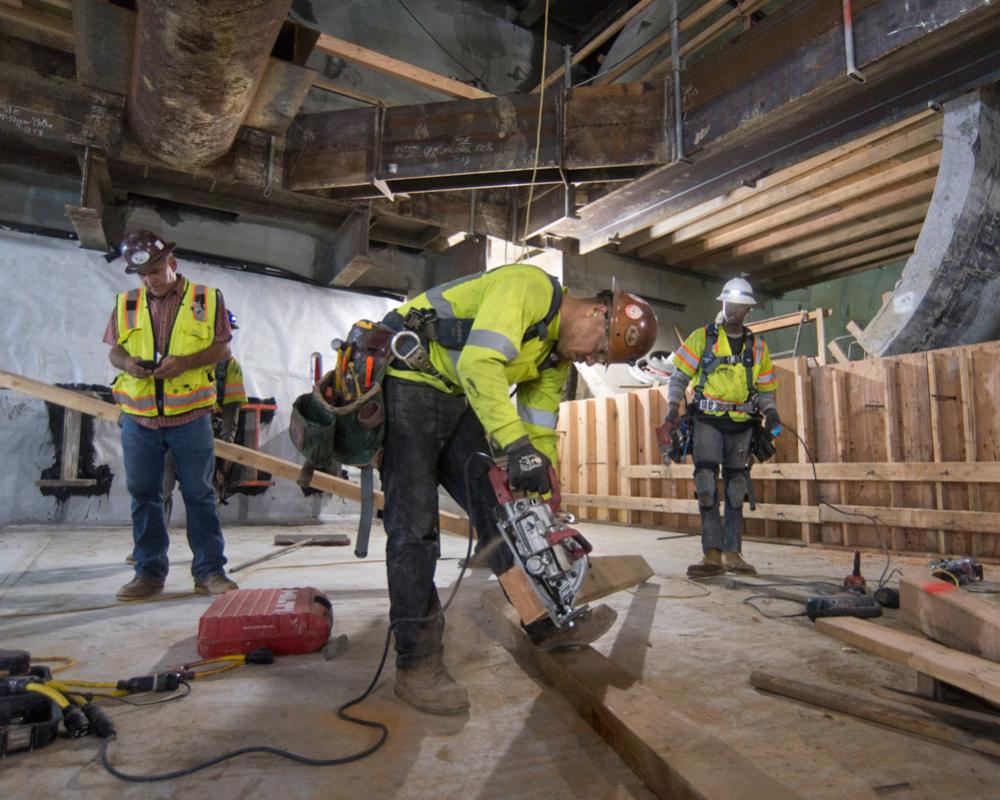 Carpenters cut boards to build cross-bracing as part of concrete form construction at the south headwall of the UMS station box.