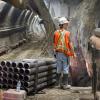 Drill casings surround a worker pausing for a bulldozer to pass during excavation of the Chinatown Station platform cavern.