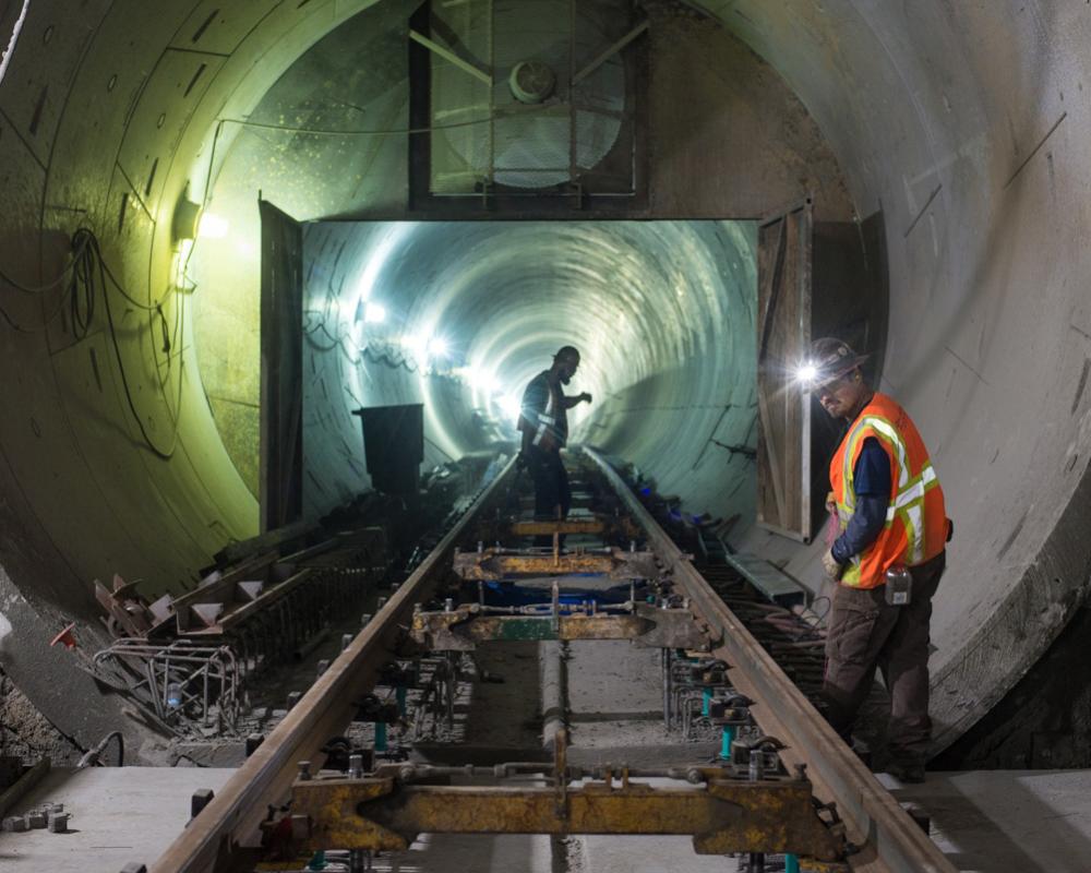 Workers check rail spacers, mounting bolts, and rebar as preparation before pouring concrete for future track plinths at YBM.