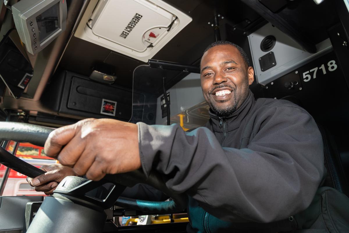 Muni operator smiling as they hold the steering wheel of a bus.