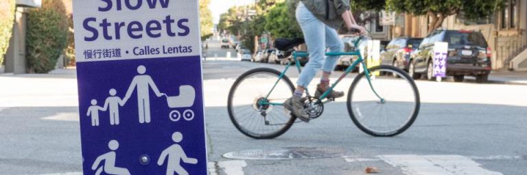 A person bikes past a Slow Street sign