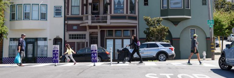 People crossing Sanchez Street. Purple Slow Streets delineators are visible.