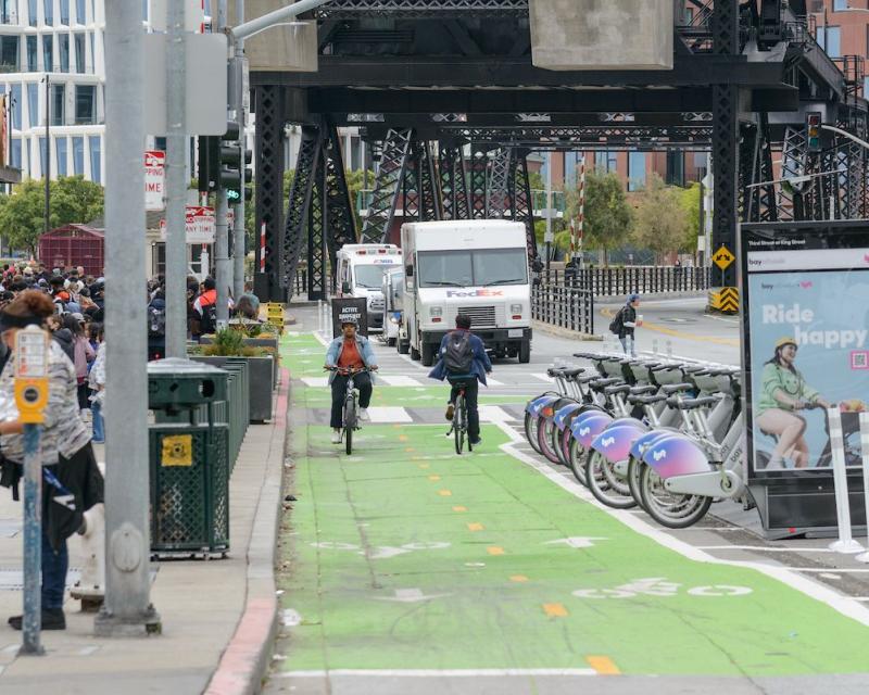 Two way green painted bike lane next to event at stadium, two bikes riding one in each direction.