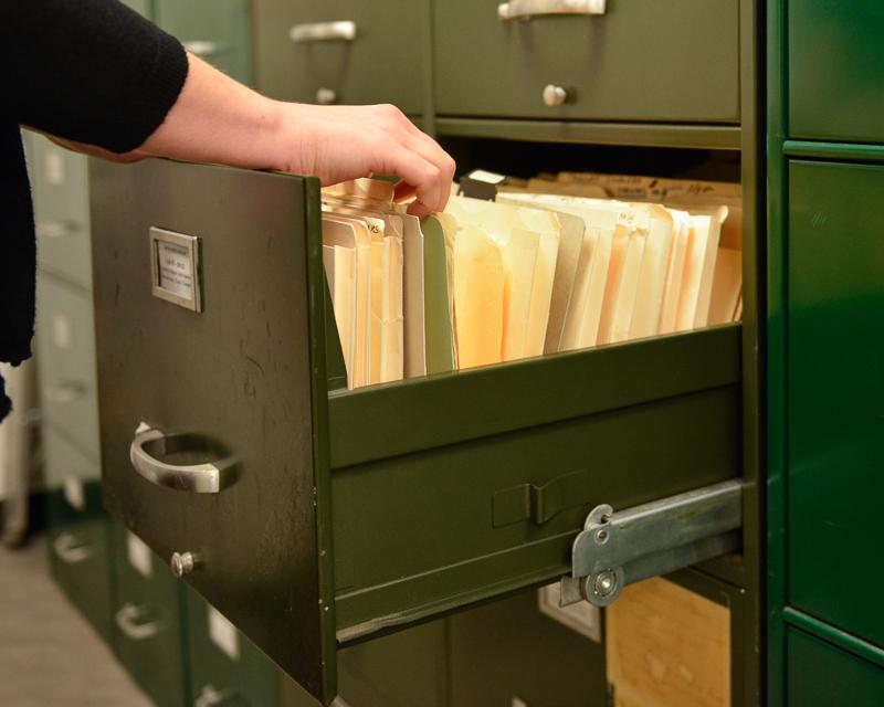 close up of hands flipping through papers in open filing cabinet drawer