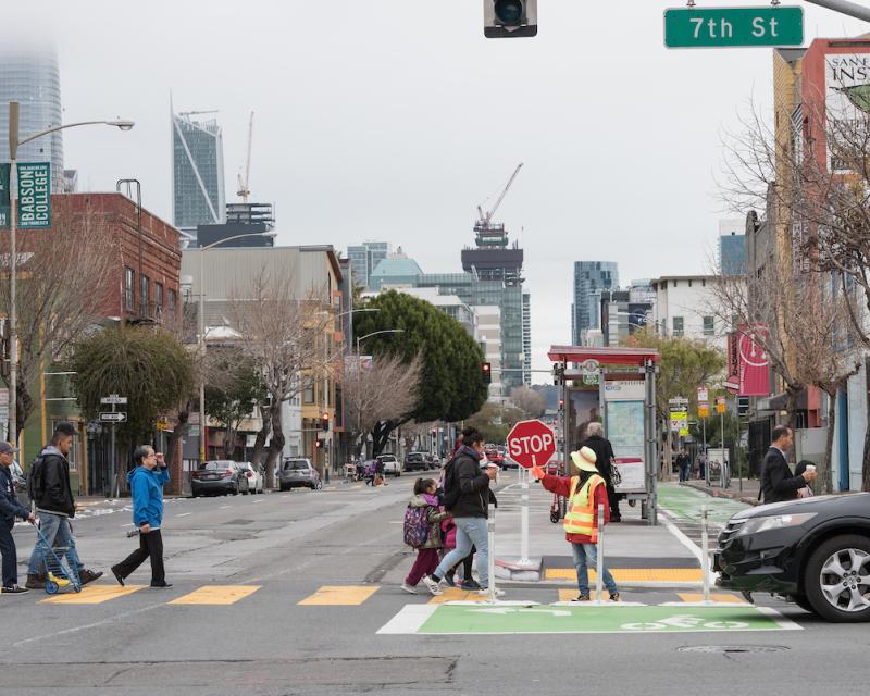 Pedestrians crossing 7th Street at Folsom Street and a school crossing guard assisting