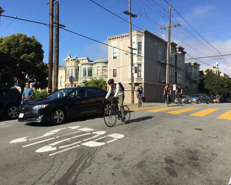 View of Page Street at Webster looking west. Eastbound cyclists are navigating around queued vehicle traffic.