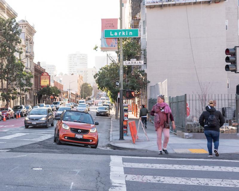 Pedestrians crossing Larkin Street as cars pass on Geary 