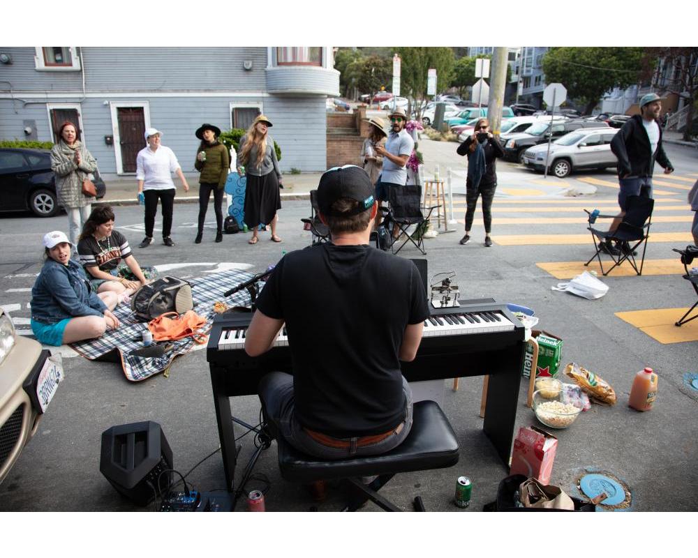 Community members on Page Slow Street stop and listen to a man playing piano in the street