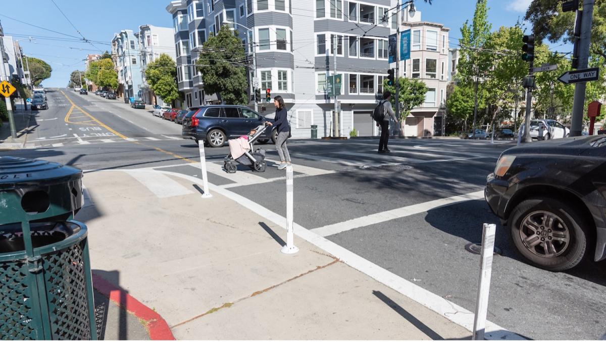 pedestrians cross turk street, where there's  a painted safety zone that extends out from the curb