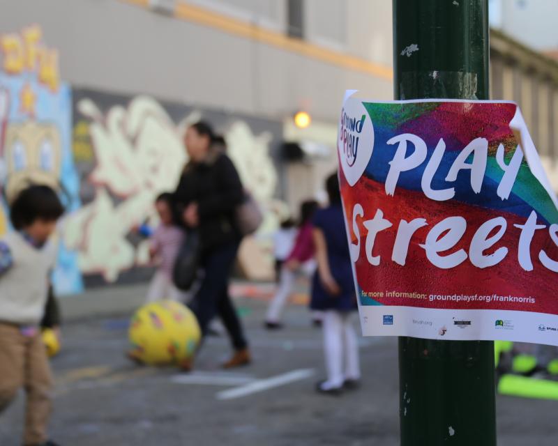 Play Streets event with colorful flyer in the foreground and children playing in the background