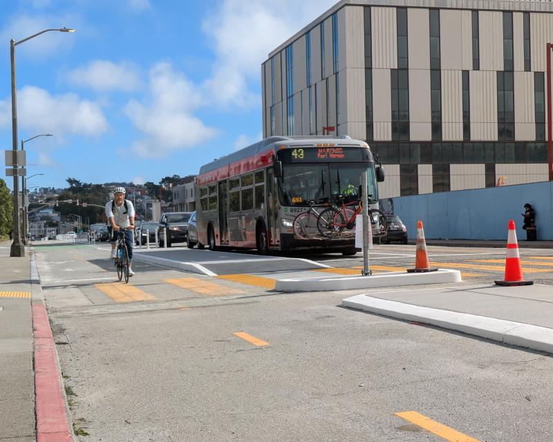 A person biking and bus travelling north on Frida Kahlo Way.