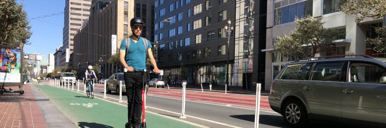 A person wearing a helmet rides a scooter in a bike lane