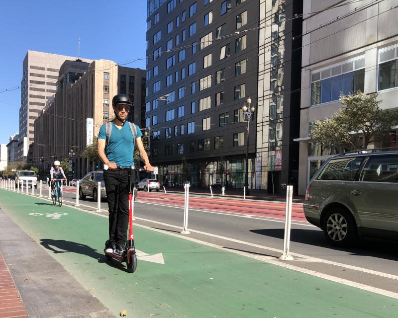 A person wearing a helmet rides a scooter in a bike lane