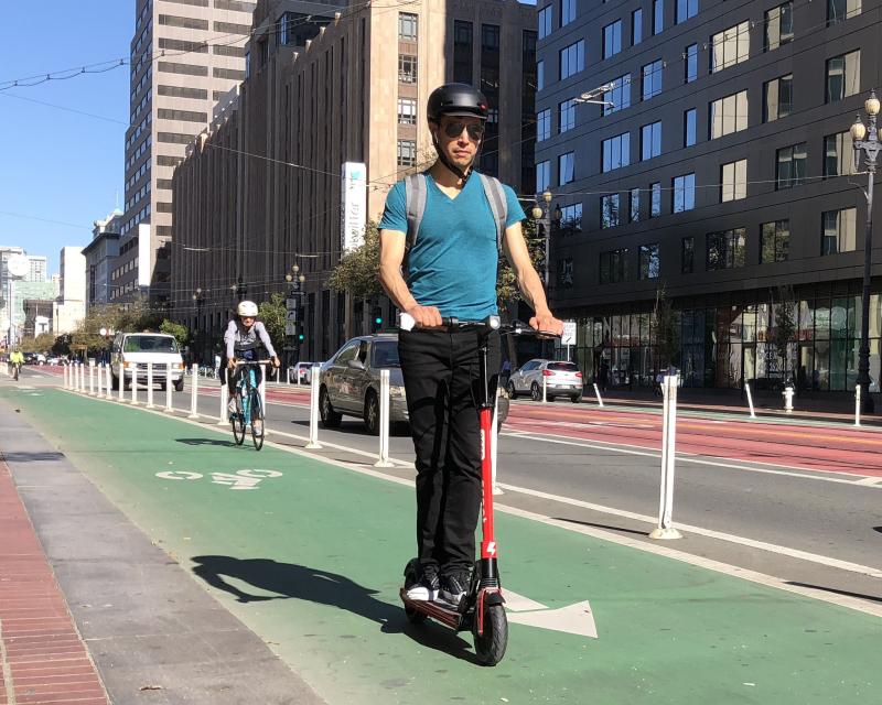 A person wearing a helmet rides a scooter in a bike lane