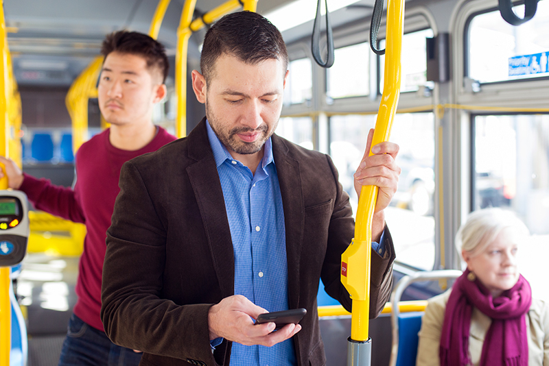 Transit riders inside of a hybrid bus Muni buslook at their mobile phones while riding.